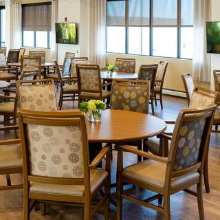 A well-lit dining room with round tables and cushioned chairs, decorated with small vases of flowers.