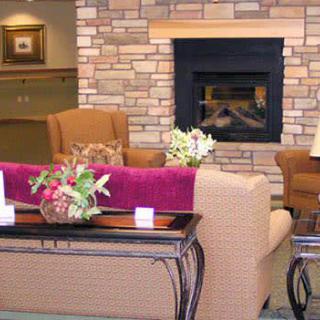 A cozy living room interior featuring a fireplace, comfortable sofas, chairs, and floral decorations.