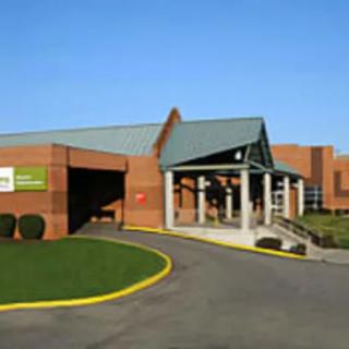 A brick building with a green roof, featuring an entrance and driveway under a clear blue sky.