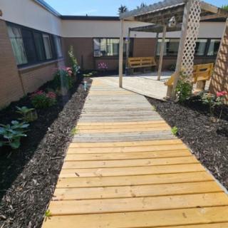 A wooden walkway leading through a garden with a pergola and outdoor seating.