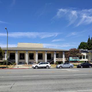 A view of a modern building with a clear blue sky and parked cars along the street.