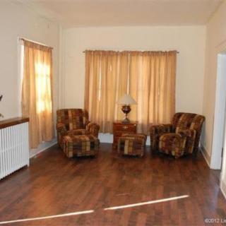 A cozy living room with patterned chairs, a small table with a lamp, and warm-colored curtains.