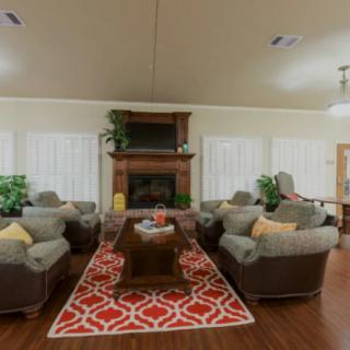 A cozy living room with multiple sofas, a coffee table, and a fireplace, accented by a vibrant red patterned carpet and green plants.