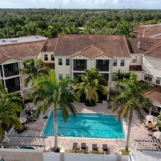 Aerial view of a residential complex with a central swimming pool surrounded by palm trees and lush greenery.