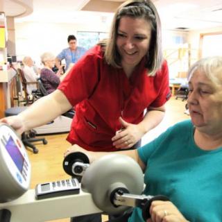 A healthcare professional assists an elderly patient with a rehabilitation exercise using specialized equipment.