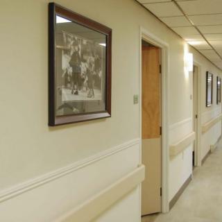 A hospital hallway with framed pictures on the wall and several doors along the corridor.