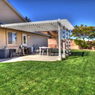 A backyard featuring a patio with a pergola, outdoor furniture, and a well-maintained grassy area.