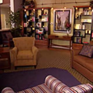 A cozy living room with comfortable chairs, a sofa, bookshelves, and artwork on the wall.