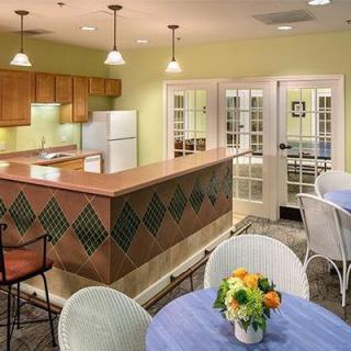A cozy kitchen and dining area featuring a counter with decorative tiles, tables with fresh flowers, and warm lighting.