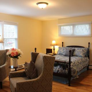 A cozy bedroom with a bed, two chairs, and a flower vase.