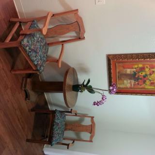 A cozy corner with wooden chairs and a table, decorated with an orchid and a colorful painting.