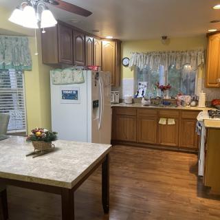 A cozy kitchen with wooden cabinets and a dining table, featuring bright lighting and decorative plants.