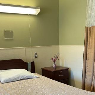 A hospital room with a neatly made bed, nightstand, and serene lighting.