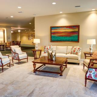 A spacious and elegantly decorated living room with a sofa, chairs, and a coffee table, complemented by a large painting and lamps.