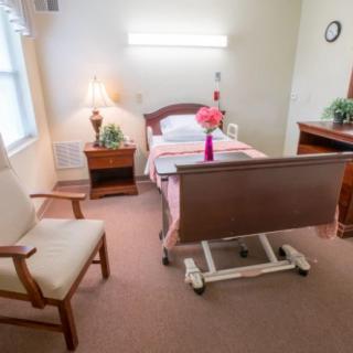 A cozy hospital room with a bed, chair, and flowers on the table.
