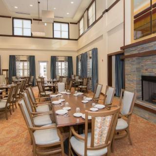 A spacious dining room with multiple tables and chairs, featuring a fireplace and large windows.