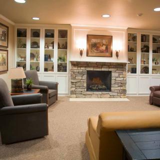 A cozy living room with armchairs, a stone fireplace, and built-in shelving.