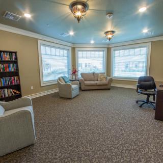 A cozy living room with sofas, armchairs, a bookshelf, and large windows.