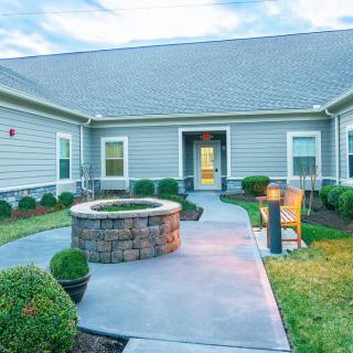 A well-maintained backyard with a stone fire pit and a paved pathway leading to the house.