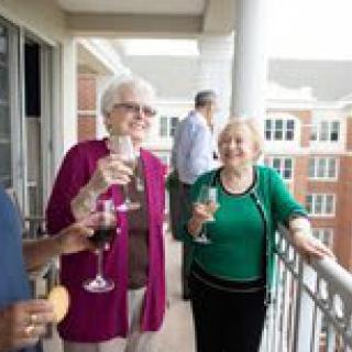 A group of elderly individuals enjoying a social gathering on a balcony, holding glasses of wine.