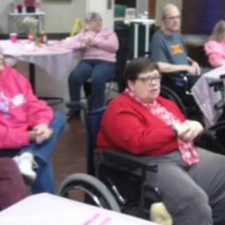 A group of people seated indoors, some in wheelchairs, engaged in a casual setting.