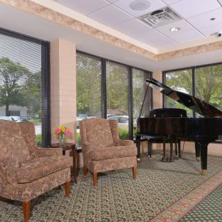 A cozy lobby area featuring a grand piano and two upholstered chairs by large windows.