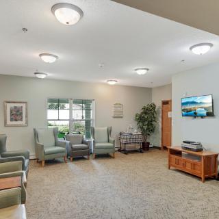 A cozy waiting room with comfortable chairs, a television, artwork on the walls, and soft lighting.
