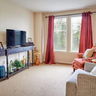 A cozy living room with a television, comfortable seating, and natural light streaming through the windows.