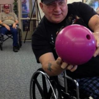 A person in a wheelchair holding a bowling ball, preparing to play indoors.