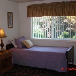 A cozy bedroom with a single bed, pillows, and a bedside lamp beside a window.