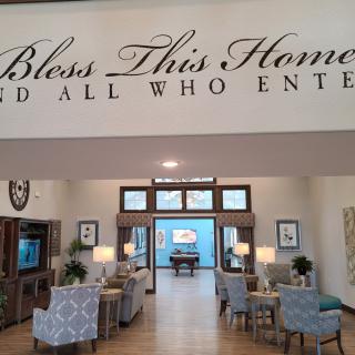 A cozy living area with a welcoming message above, 'Bless This Home and All Who Enter.'