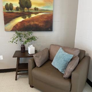 A cozy corner featuring a comfortable armchair, decorative cushions, and a serene landscape painting.