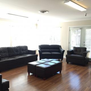 A bright living room with a set of dark leather furniture and hardwood floors.