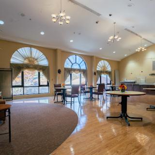 A spacious and inviting lounge area with large windows, furnished with tables and chairs, providing a warm atmosphere.