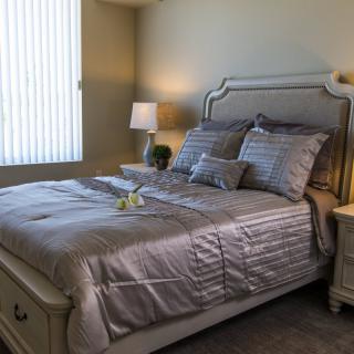 A well-appointed bedroom with a stylish bed set, including silky gray bedding, matching pillows, and a nightstand with a lamp.
