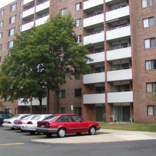 A view of a multi-story apartment building with a parking lot in front.