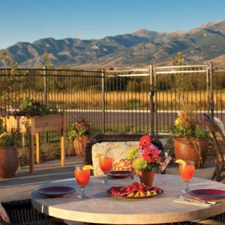 A scenic outdoor patio with a view of mountains, featuring a nicely set table with drinks and flowers.