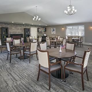 A spacious dining room with multiple tables and chairs, featuring elegant chandeliers and a carpeted floor.