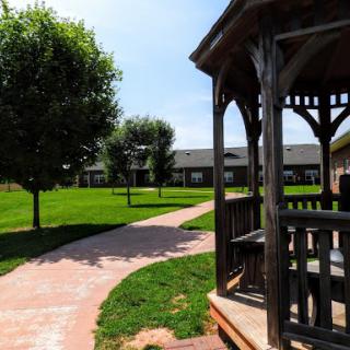 A serene view of a park showcasing a gazebo, manicured grass, and a winding pathway under a clear blue sky.