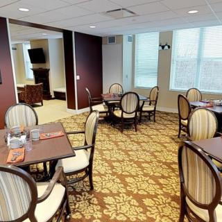 A cozy dining area with elegant tables and chairs, featuring a patterned carpet and large windows.