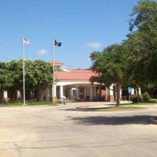 A building entrance with flags and trees under a clear blue sky.