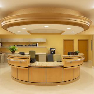 A modern reception area featuring a wooden desk, bright lighting, and yellow walls.