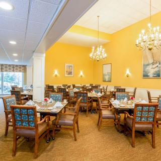 A well-lit dining room with elegant chandeliers and neatly arranged tables and chairs.
