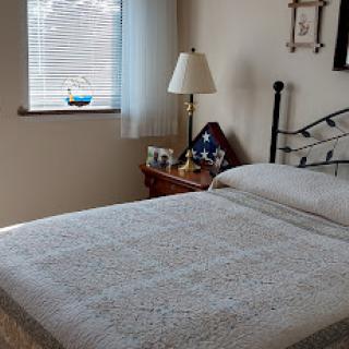A cozy and well-lit bedroom featuring a neatly made bed, a bedside lamp, and decorative items on the nightstand.