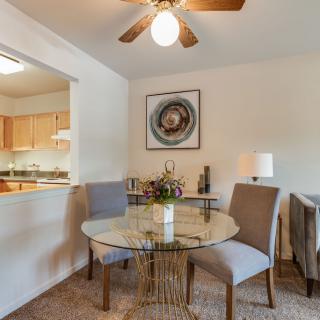 A cozy dining area with a glass table, surrounded by chairs, and decorated with artwork and a lamp.