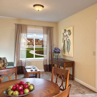 A cozy living room with a dining area featuring elegant furniture, artwork on the wall, and a window offering a scenic view.