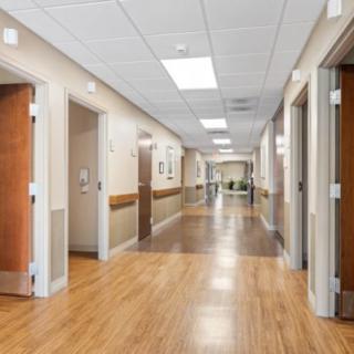 A well-lit hospital hallway with wooden floors and multiple doors leading to various rooms.