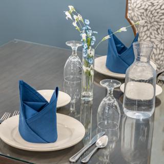 An elegant table setting featuring neatly folded blue napkins, glassware, and a small vase with flowers.
