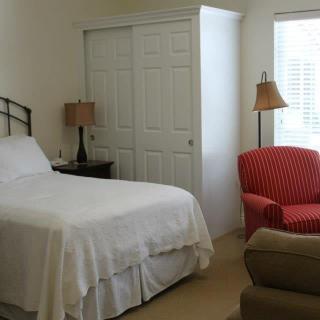 A cozy bedroom featuring a bed with white linens, a red striped armchair, and two lamps.
