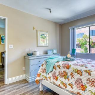A cozy bedroom with floral bedding, featuring a dresser, artwork on the wall, and a large window offering natural light.
